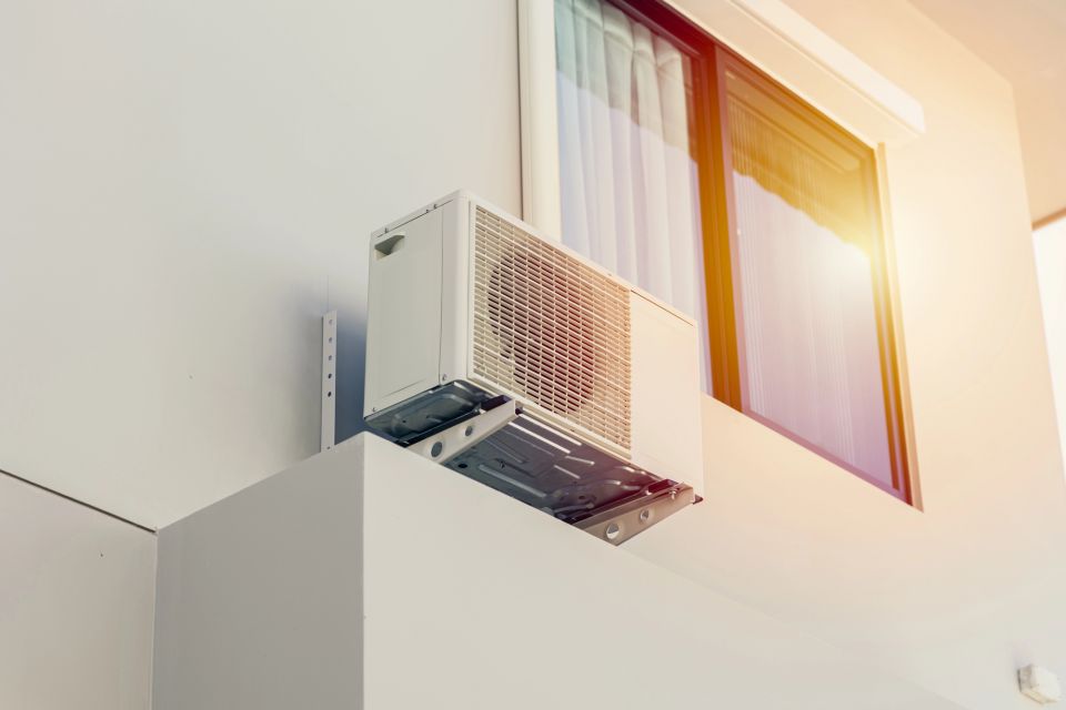 Eine Klimaaanlage steht vor der Außenfassade eines Hauses unterhalb eines Fensters.