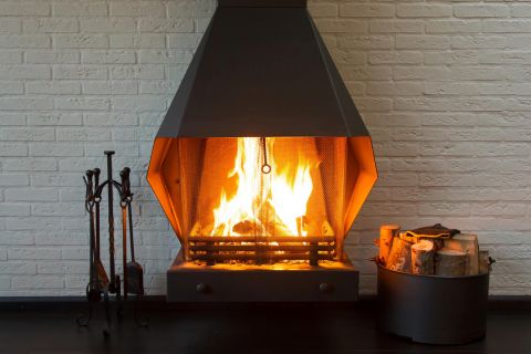 Ein offener Kaminofen steht vor einer weißen gemauerten Wand, im Ofen lodert ein Feuer.
