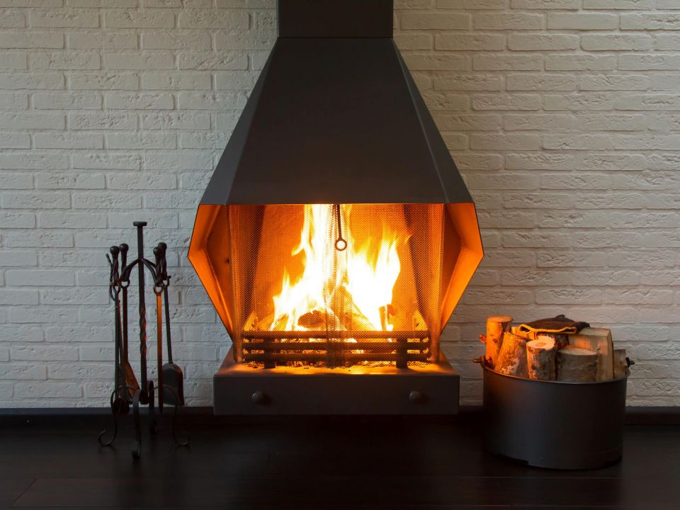 Ein offener Kaminofen steht vor einer weißen gemauerten Wand, im Ofen lodert ein Feuer.