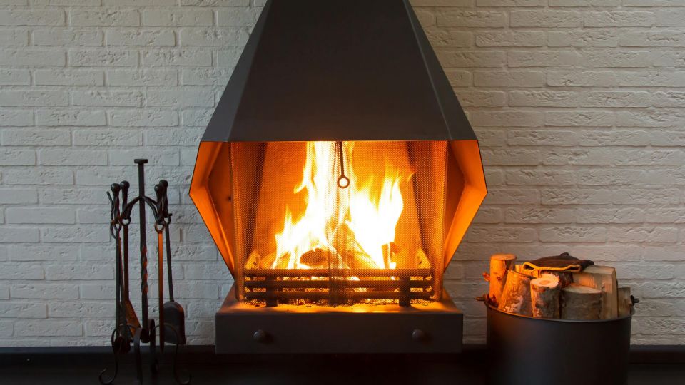 Ein offener Kaminofen steht vor einer weißen gemauerten Wand, im Ofen lodert ein Feuer.